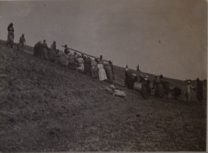 Operai al lavoro durante le fasi delicate di trasporto e traino, in un declivio in salita, di una delle pesanti casse contenenti il sarcofago del governatore Ibu. Album fotografico, Scavi Schiaparelli. 