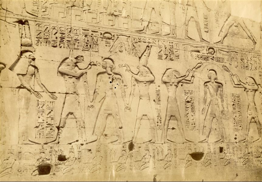 The image shows some sacred scenes carved on the walls of the first hypostyle hall of the Temple of Seti I at Abydos. His son, Ramesses II is depicted in the middle of the gods Anubis and Horus. The signature of the author is faintly visible at the bottom centre. 