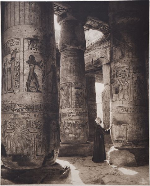 Hypostyle Hall in the Temple of Seti I at Abydos. An egyptian can be seen photographed next to a column. 