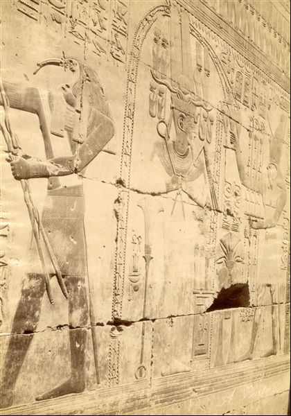 The photograph shows a detail of the texts and images from the chapel of Osiris in the Temple of Seti I at Abydos. In the scene, the god Harsiesi (right) purifies the pharaoh dressed in Osiris-like robes (centre), and on the left the god Thoth performs another ritual. The author's signature is at the bottom right.   