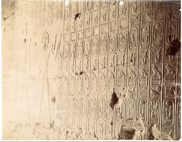 The photograph shows the scene of Ramesses II reading a papyrus scroll in front of his father Seti I and a detail of the text with the cartouches of the pharaohs from the so-called "Abydos King List", the succession of canonical dynasties that preceded Seti I. The relief is located on the western wall of the "Gallery of Ancestors" or the “Gallery of Lists” in the southern wing of the Temple. 