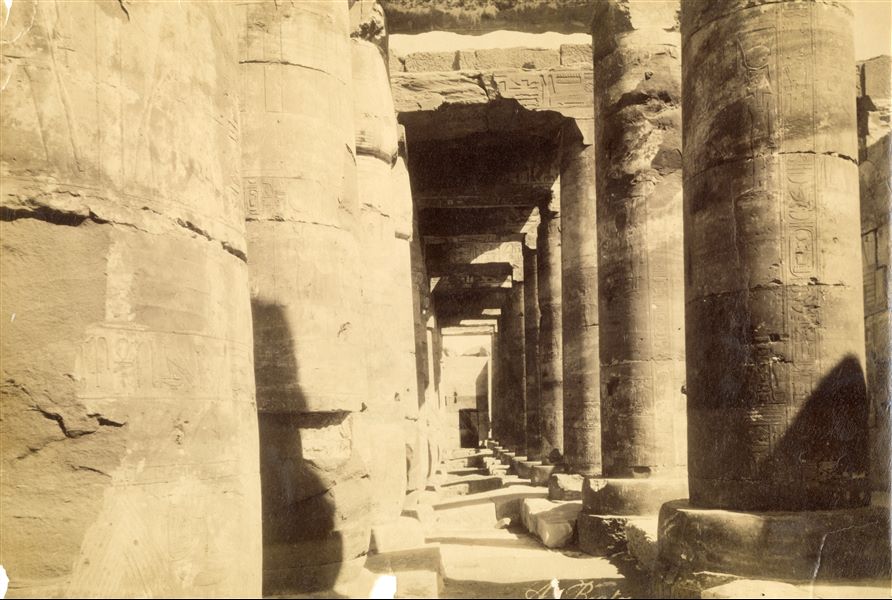 View of the colonnade of the second hypostyle hall of the Temple of Pharaoh Seti I at Abydos. At the bottom, the entrance to the "Gallery of the Ancestors" of Abydos, a long list of cartouches of rulers, from Menes/Narmer (the country's first semi-legendary ruler) to Seti I. The author's signature is at the bottom centre.  