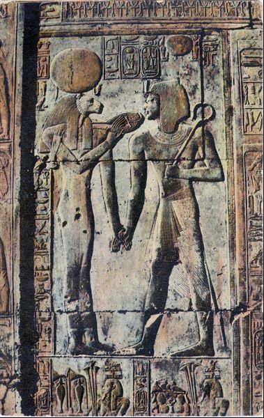 Particolare di una parete decorata dal tempio del faraone Seti I ad Abido, in cui sono presenti una divinità a testa leonina a sinistra, e il faraone a destra. L’immagine risulta colorata a posteriori. Album “Cartes postales”